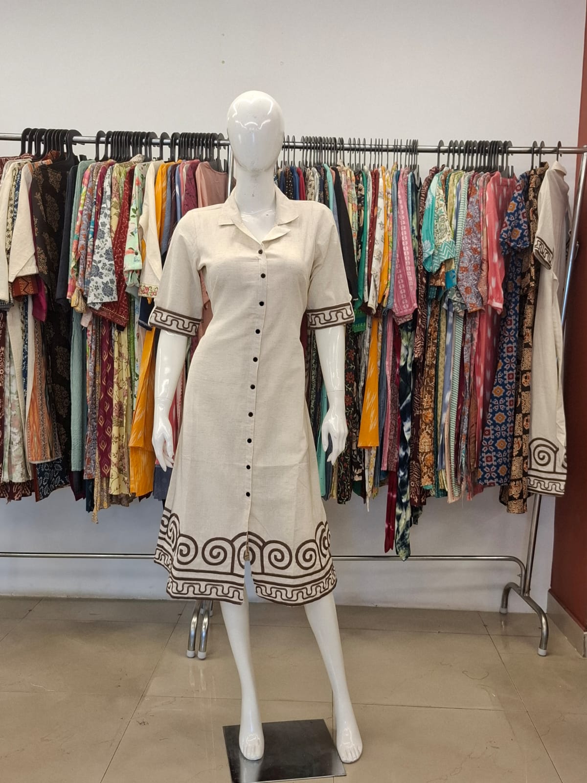 Mannequin wearing a cream dress with black patterns in a clothing store setting.