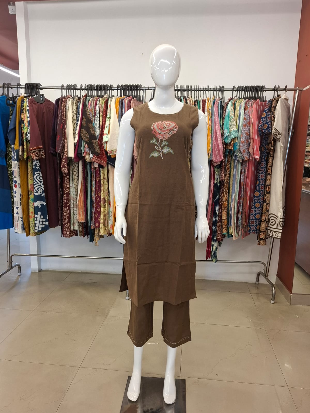 Mannequin wearing a brown dress with floral embroidery in a clothing store.