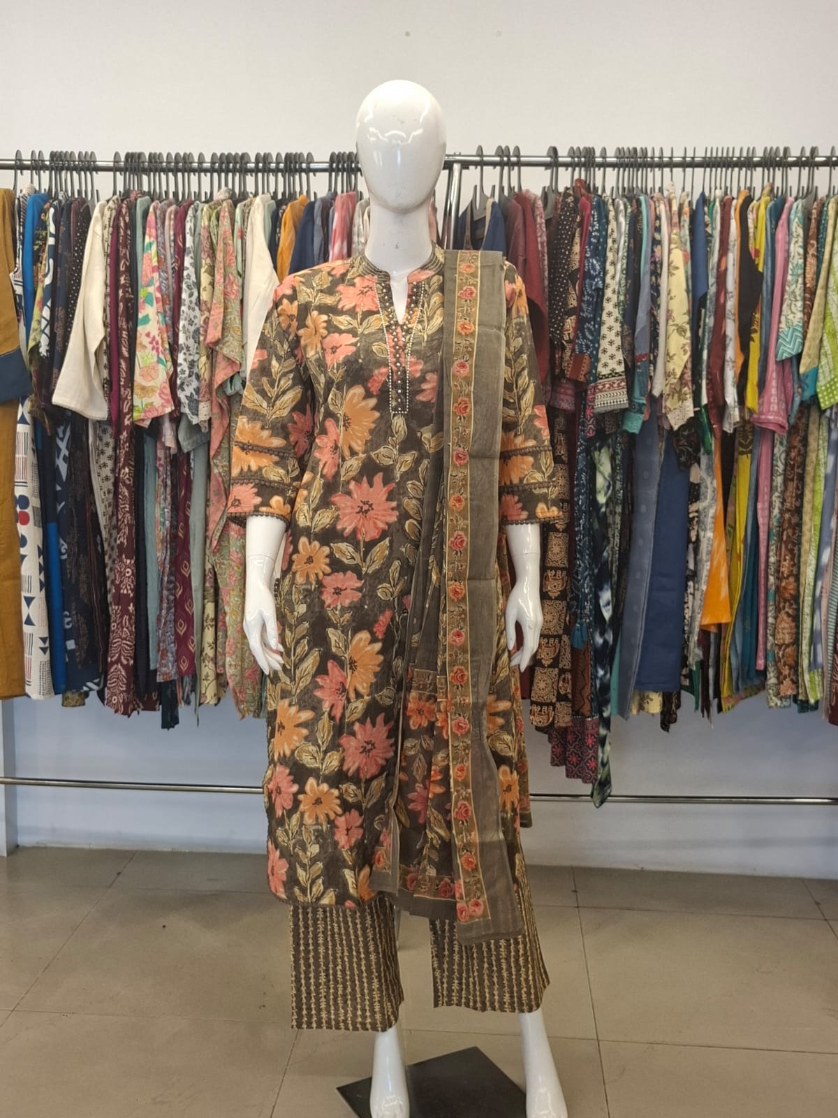 Mannequin wearing a floral dress with a patterned scarf in front of a rack of clothes.