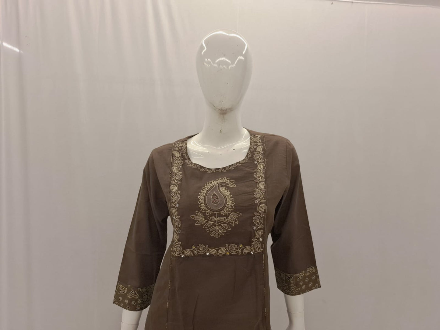 Brown dress with gold embroidery on a mannequin against a plain background