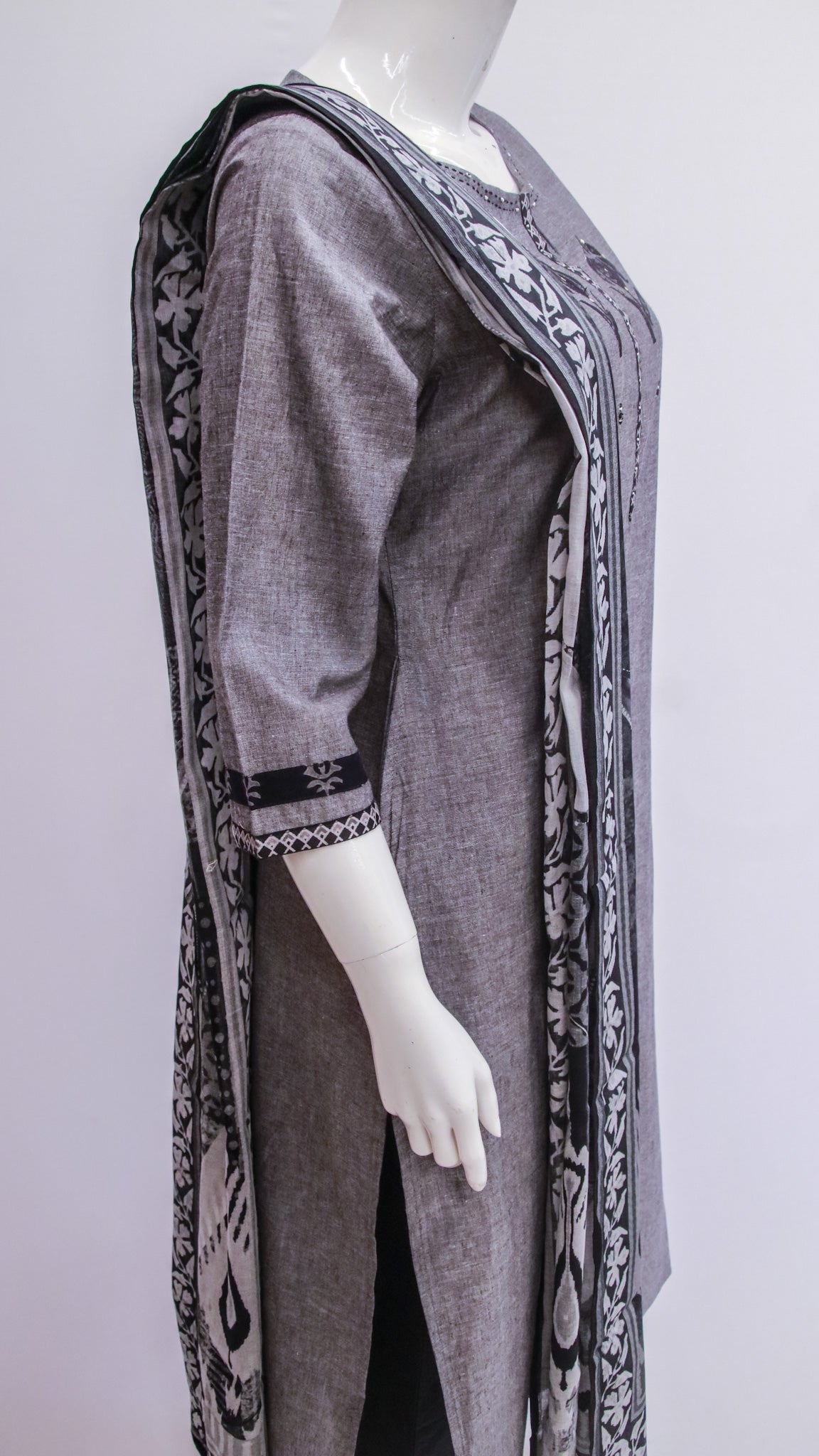 Long, dark gray dress with intricate patterns on a mannequin against a white background