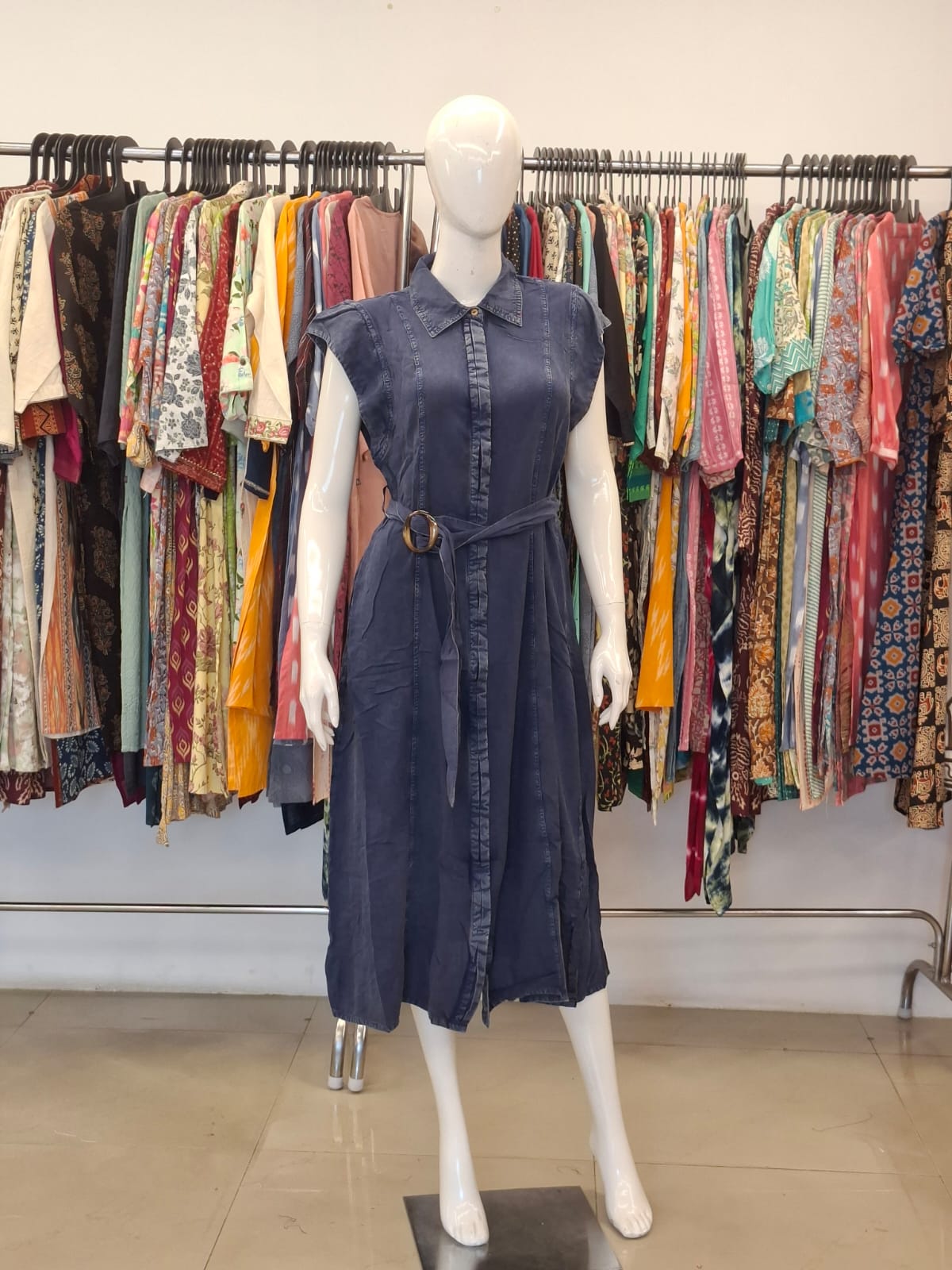 Mannequin wearing a navy dress in front of a rack of colorful clothing.