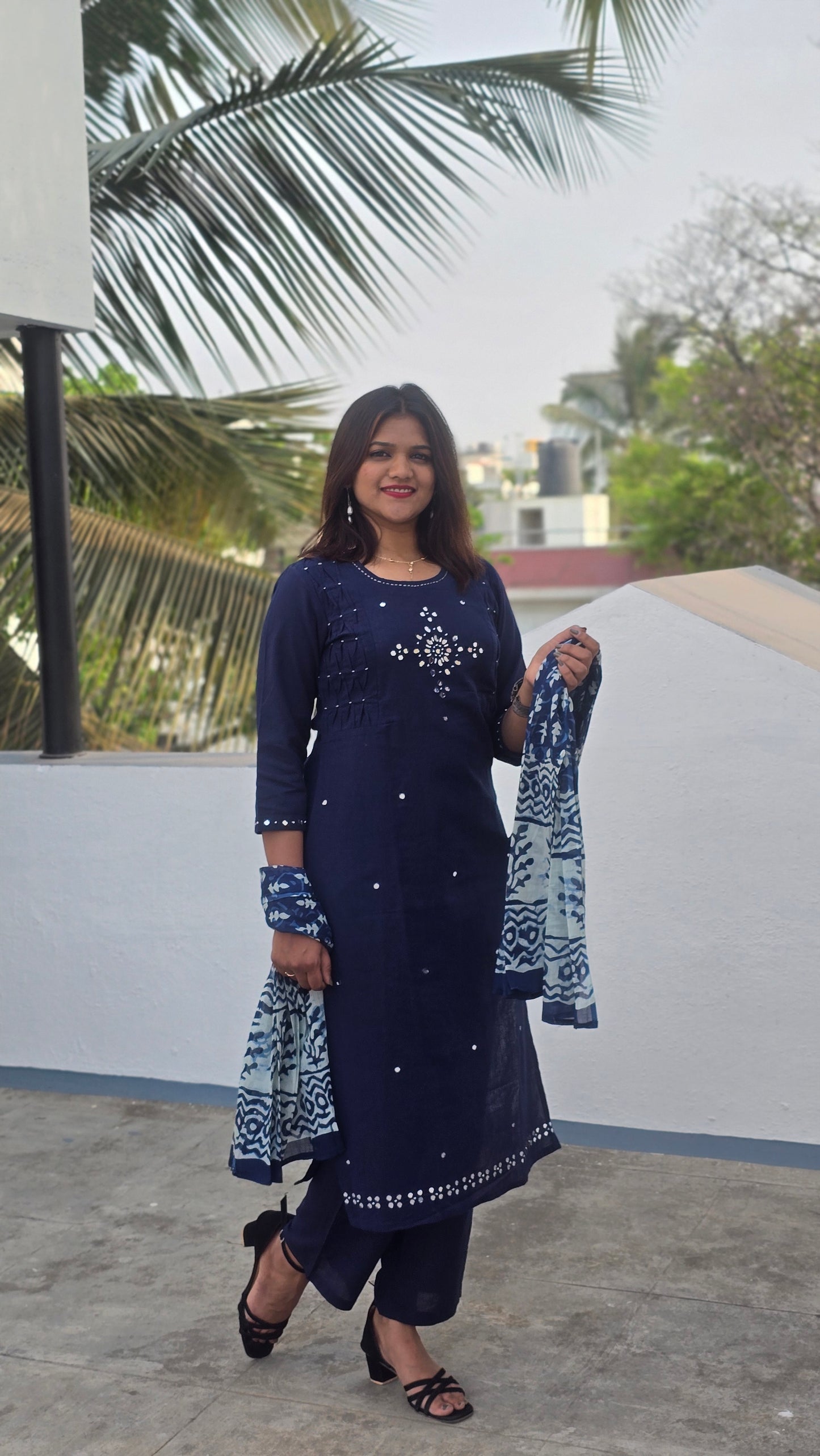 Woman in a blue outfit standing outdoors with palm trees in the background