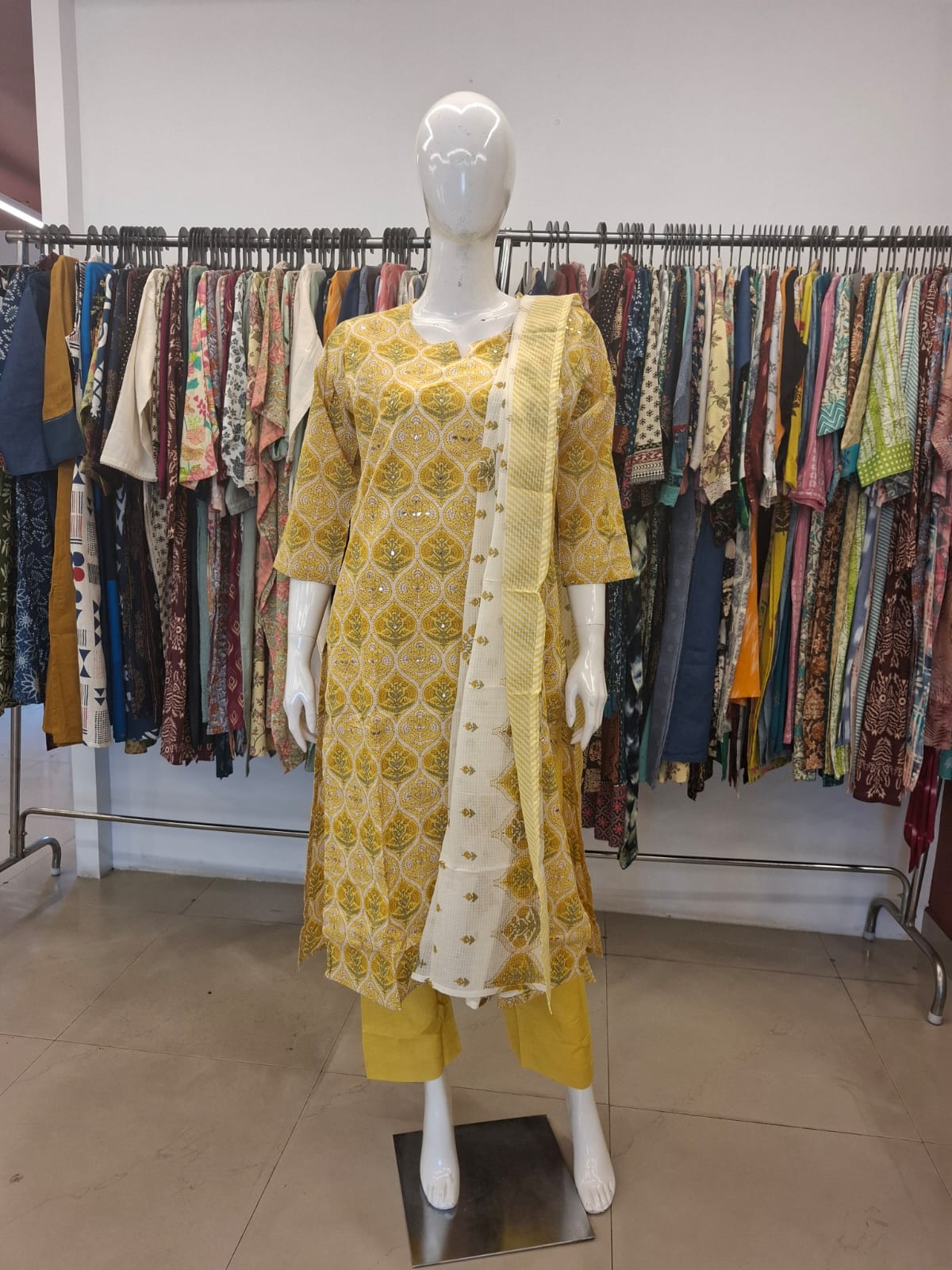 Mannequin wearing a yellow and white outfit with a patterned shawl in a clothing store.