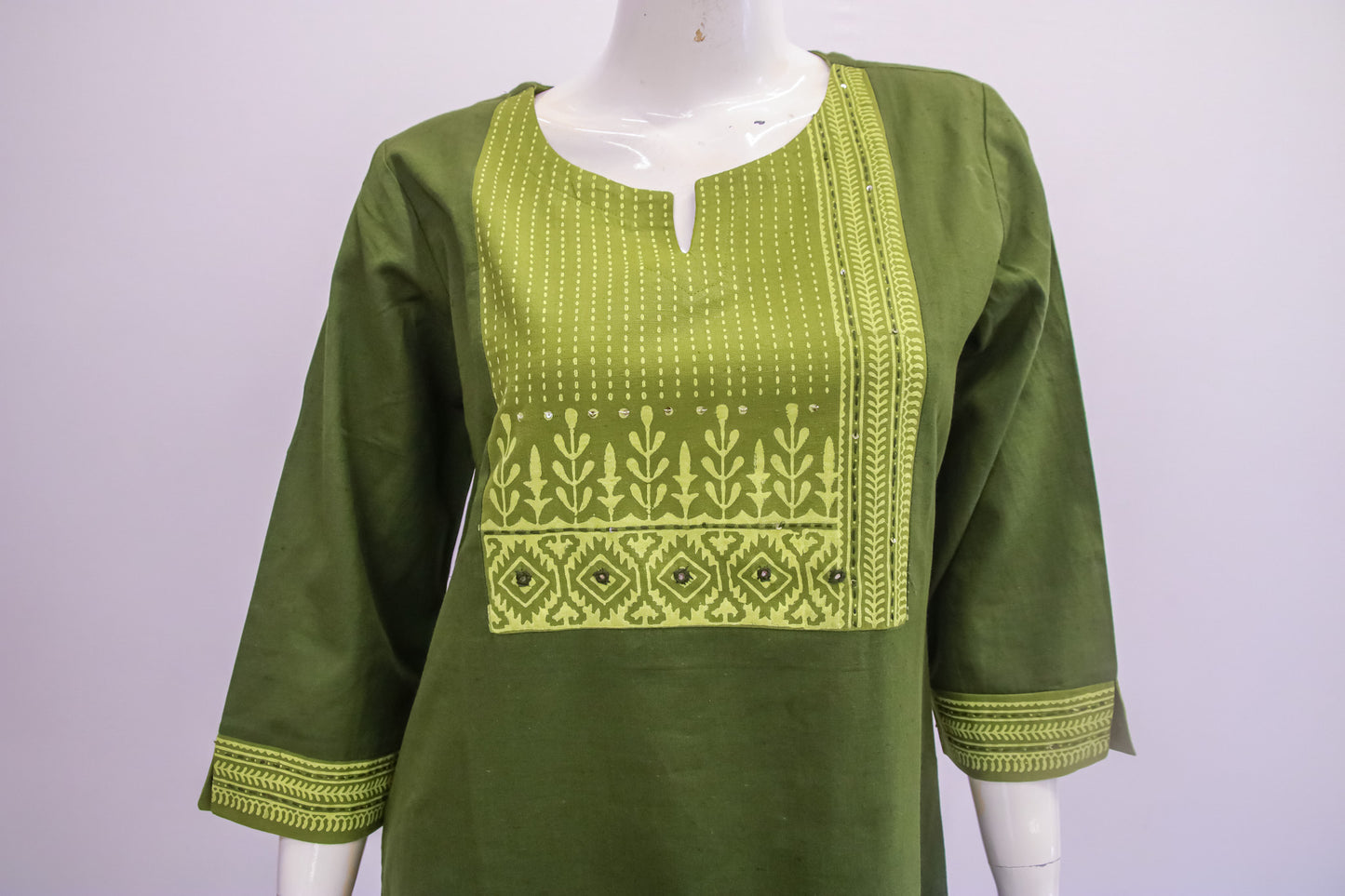 Green embroidered top on a mannequin against a white background