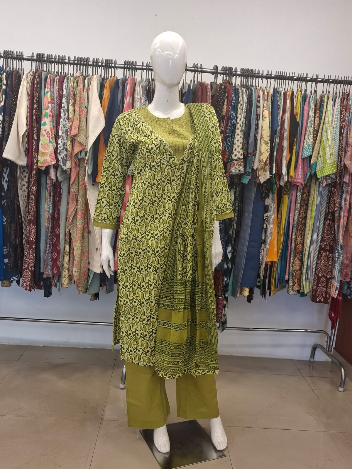 Mannequin wearing a green patterned outfit with a matching shawl in a clothing store.