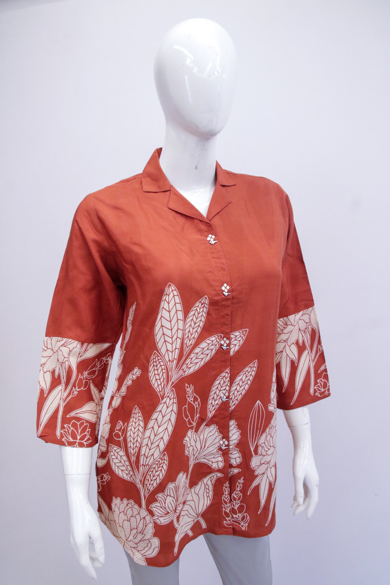 Red shirt with white floral pattern on a mannequin against a white background