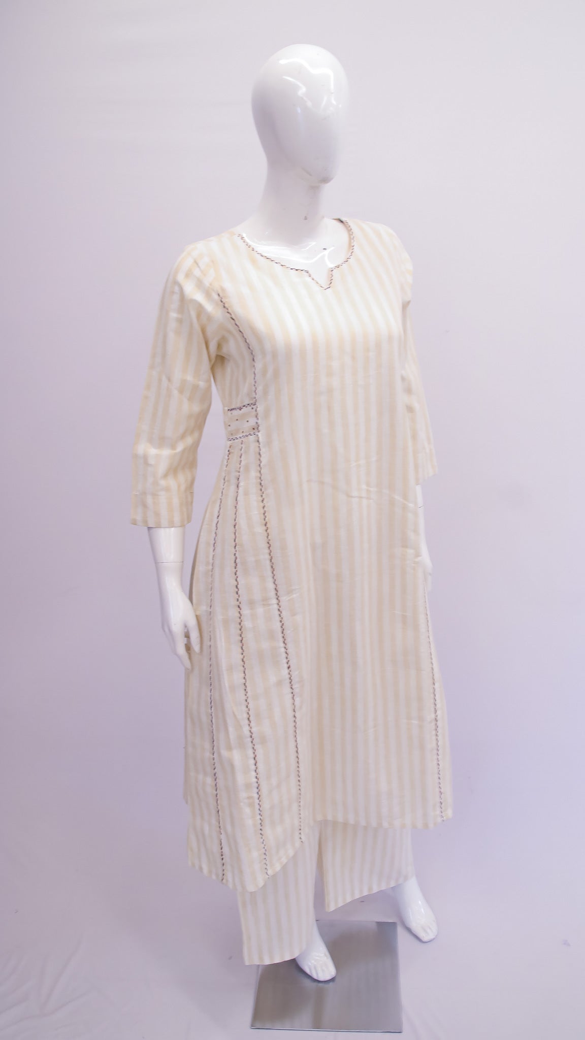 Mannequin wearing a long, light-colored dress with a subtle pattern on a plain background