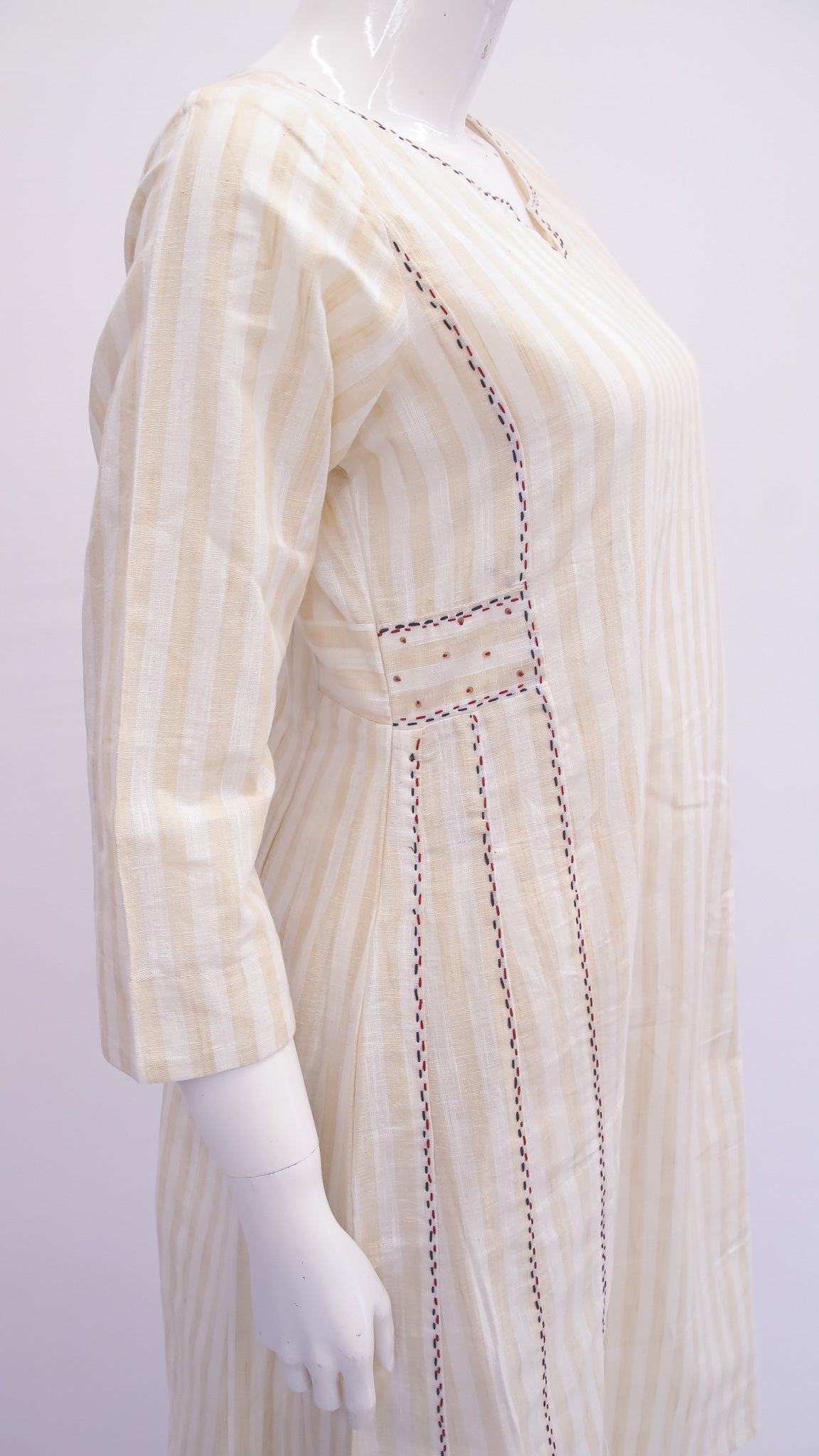 Mannequin wearing a beige and white striped dress with intricate detailing on a white background