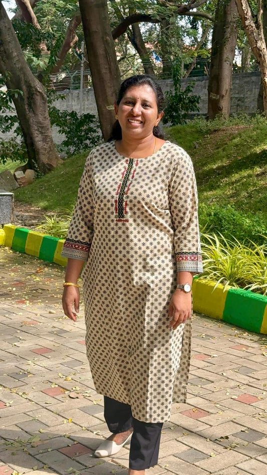 Woman in a patterned kurta standing outdoors on a paved path with greenery in the background