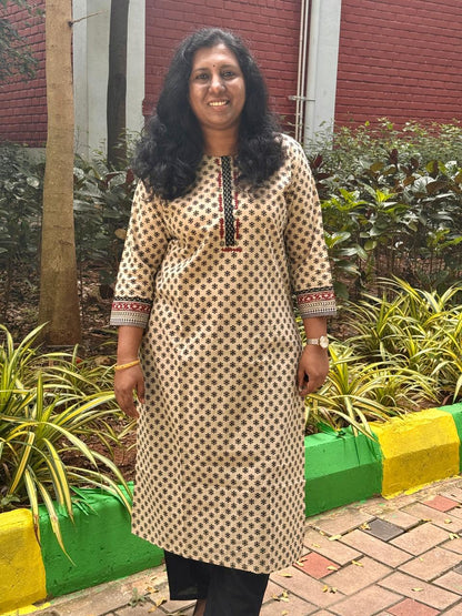 Woman in a patterned kurta standing outdoors with plants and a building in the background
