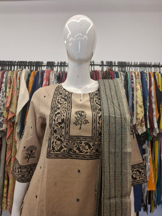 Mannequin wearing a beige embroidered outfit with a patterned scarf against a background of colorful fabrics.