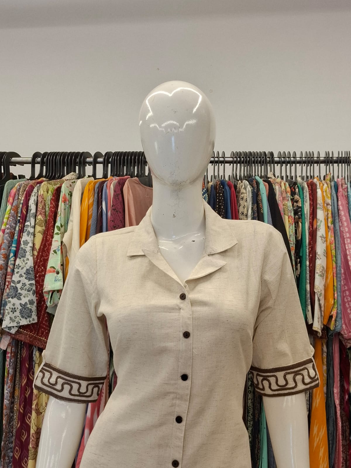 Mannequin wearing a beige shirt with decorative sleeves in a clothing store.