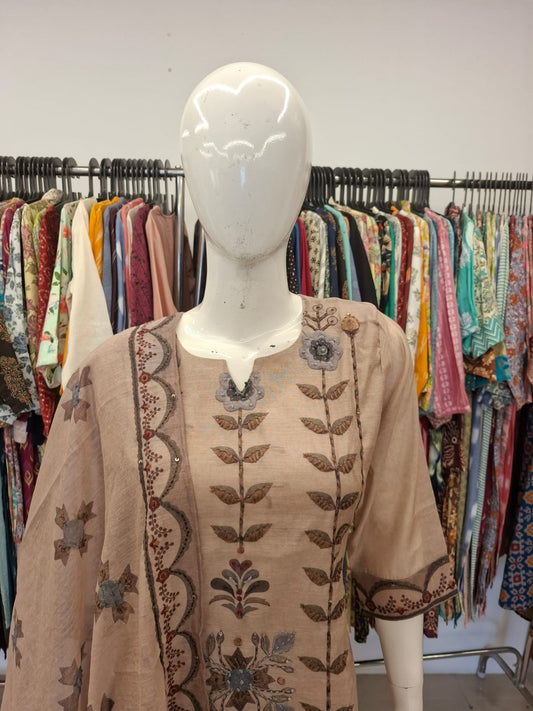 Mannequin wearing a beige embroidered top with floral patterns against a background of clothing racks.