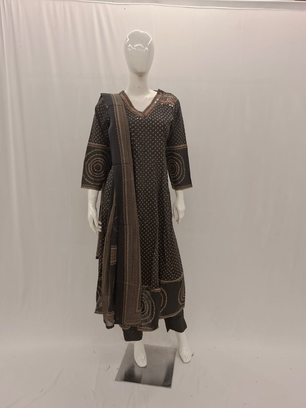 Mannequin wearing a brown patterned outfit with a long scarf on a white background