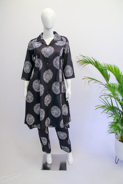 Black patterned outfit on a mannequin with a white background and plant