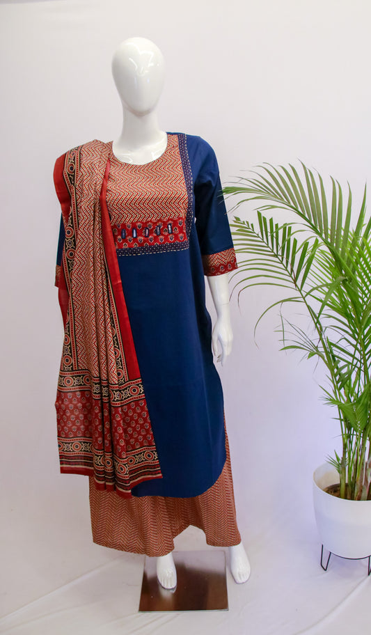 A mannequin displaying a blue cotton ajrakh dupatta set with a kurta and pant, standing in front of a white background with a potted plant to the side.
