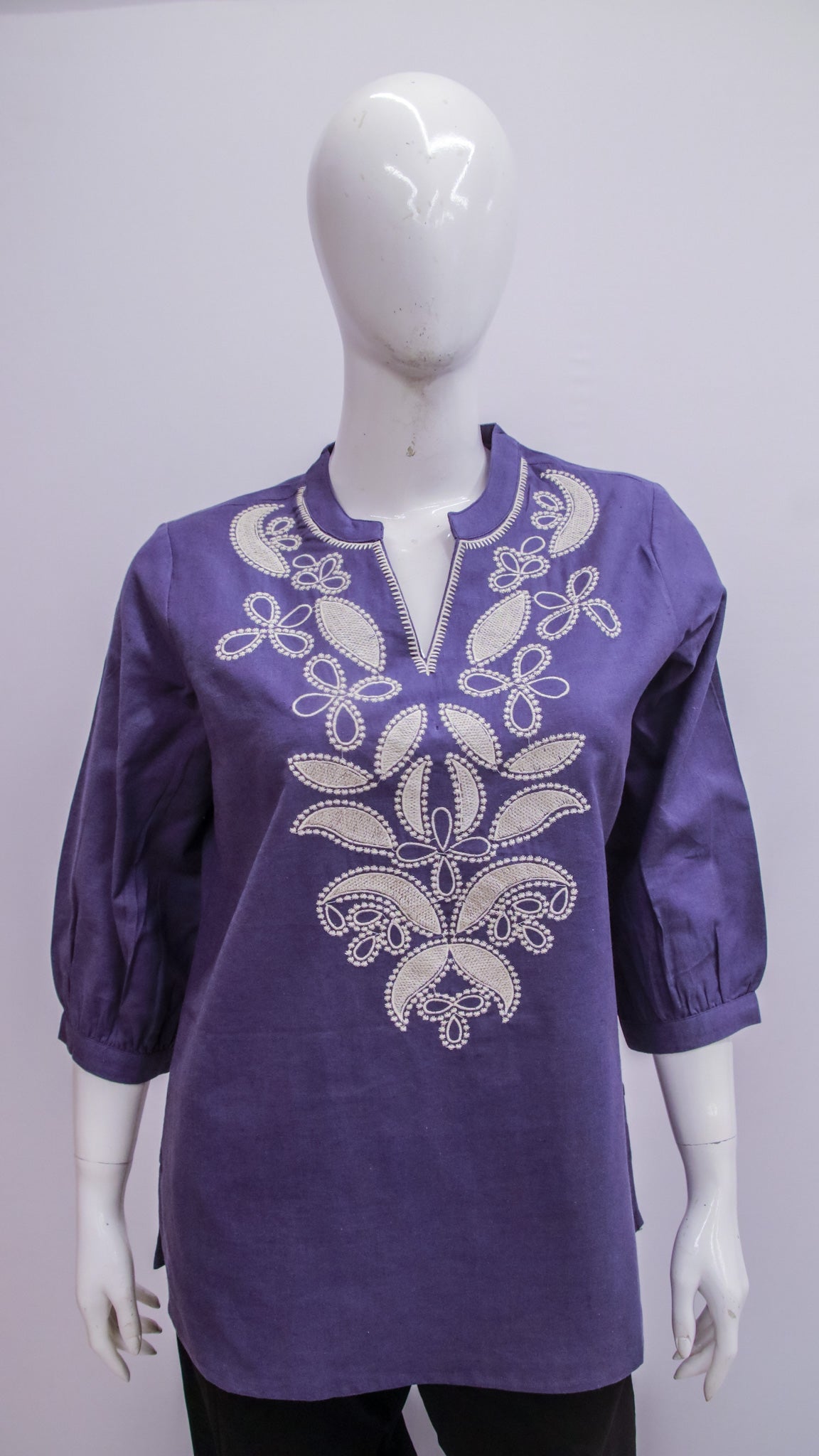 Purple blouse with white embroidery on a mannequin against a gray background
