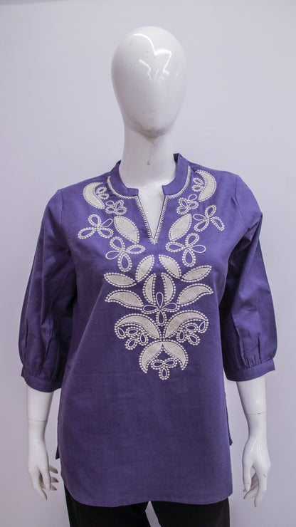 Purple blouse with white embroidery on a mannequin against a gray background