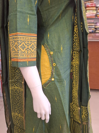 Green traditional outfit with yellow patterns on a mannequin in a store setting.