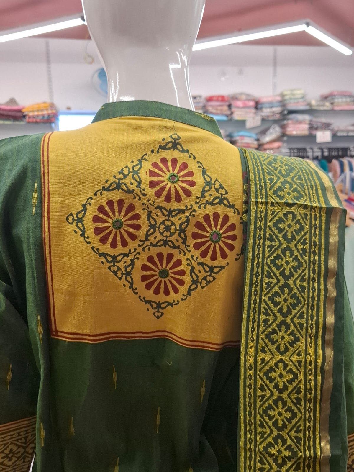 Traditional green and yellow embroidered garment on a mannequin in a store setting.
