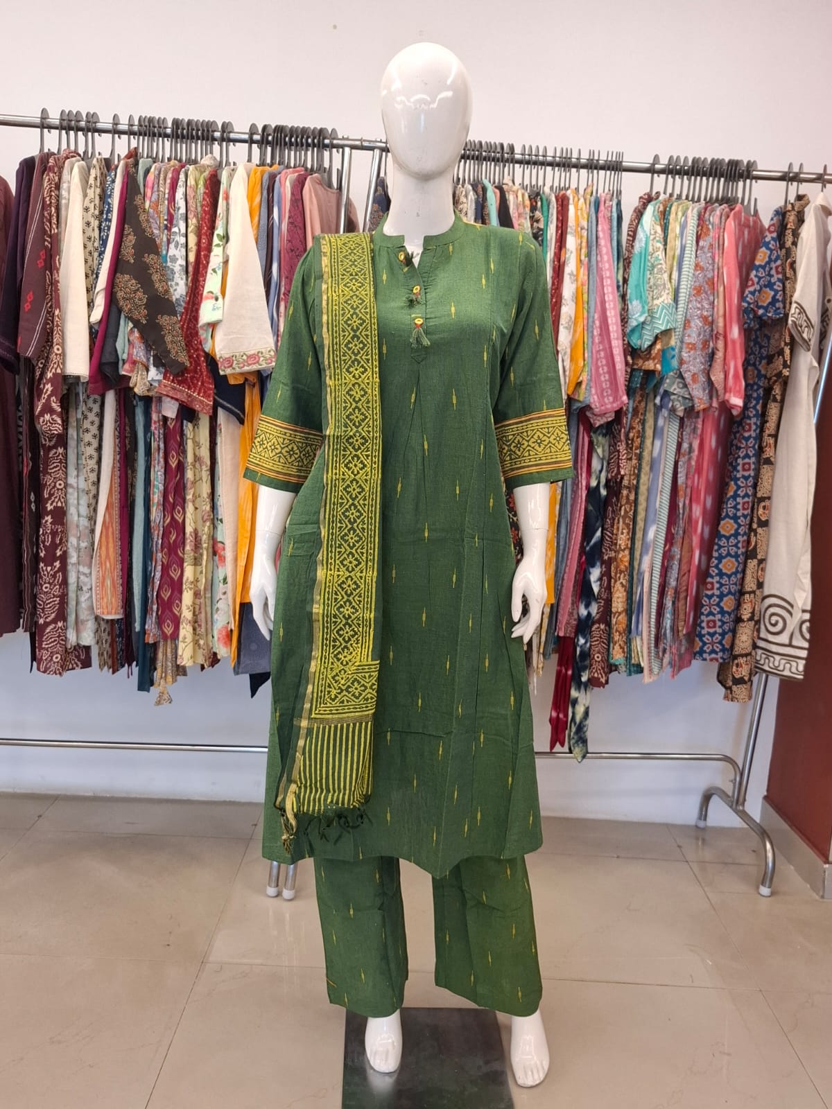 Green traditional outfit with a matching dupatta on a mannequin against a clothing rack background.