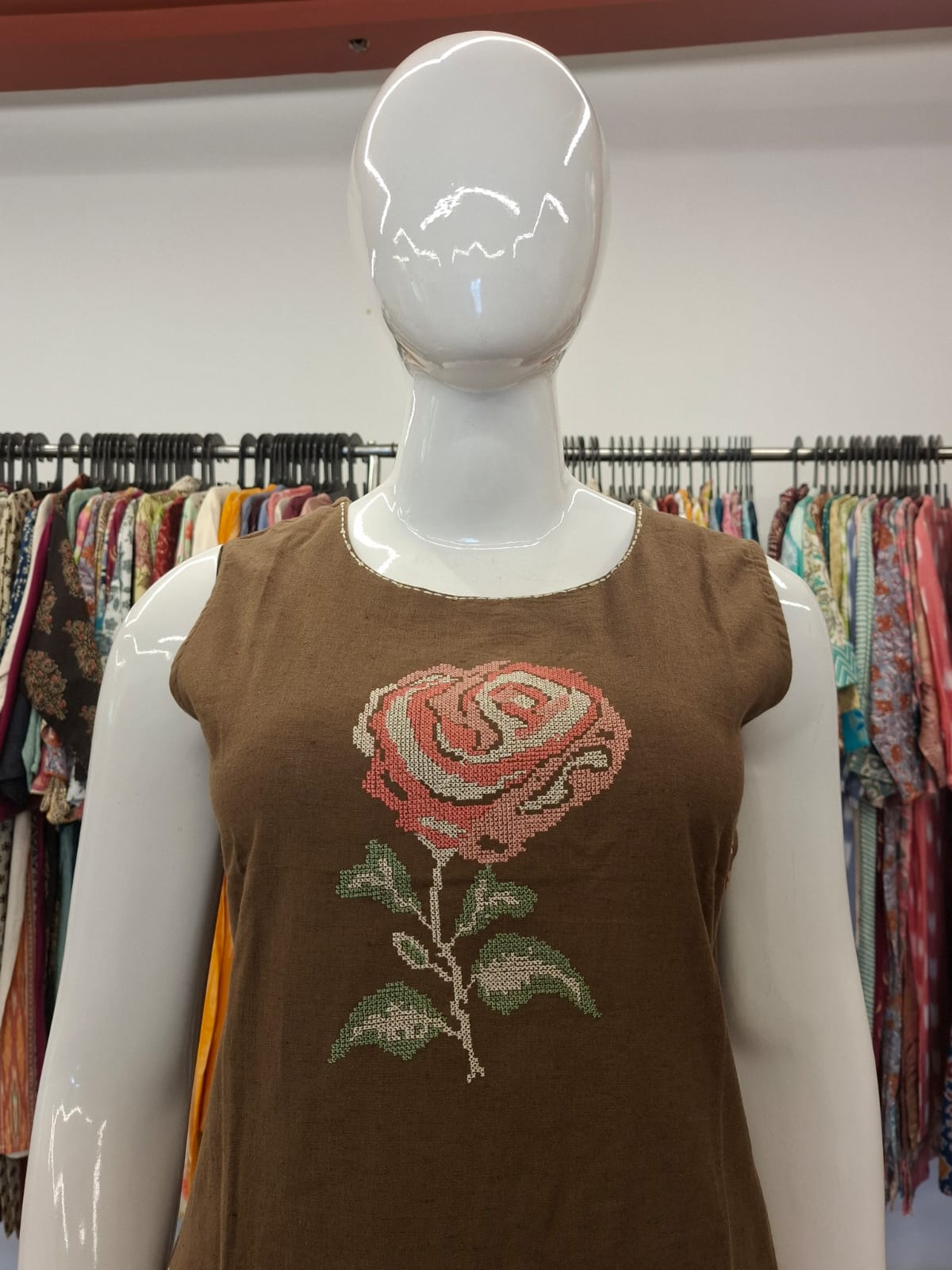 Mannequin wearing a brown sleeveless top with a rose design in a clothing store.