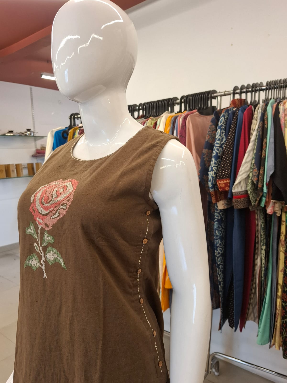 Mannequin wearing a brown sleeveless top with floral embroidery in a clothing store.