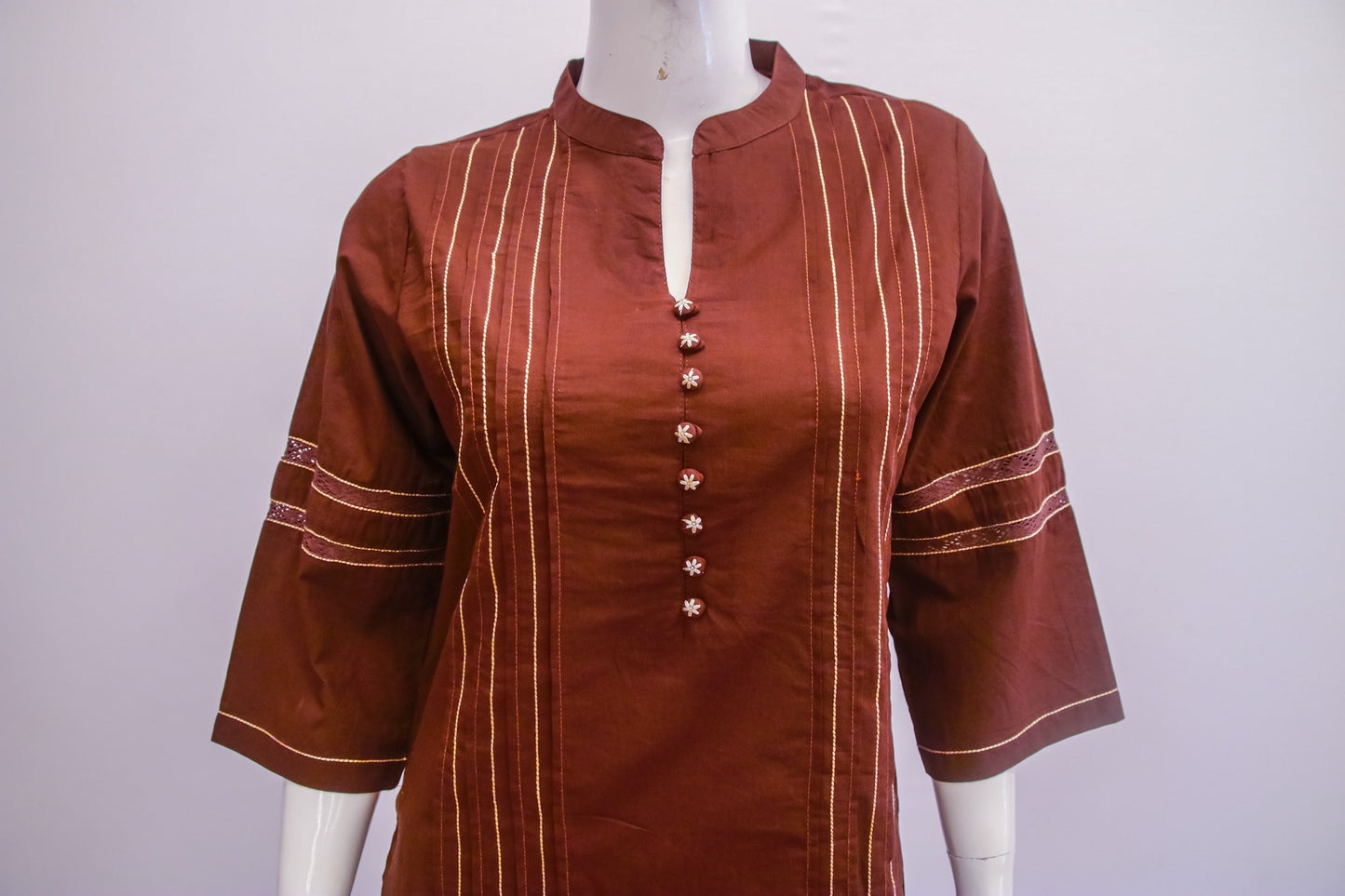 Brown shirt with white embroidery on a mannequin against a white background