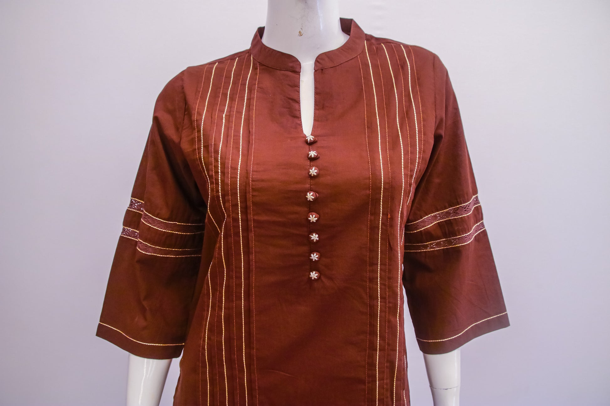 Brown shirt with white embroidery on a mannequin against a white background