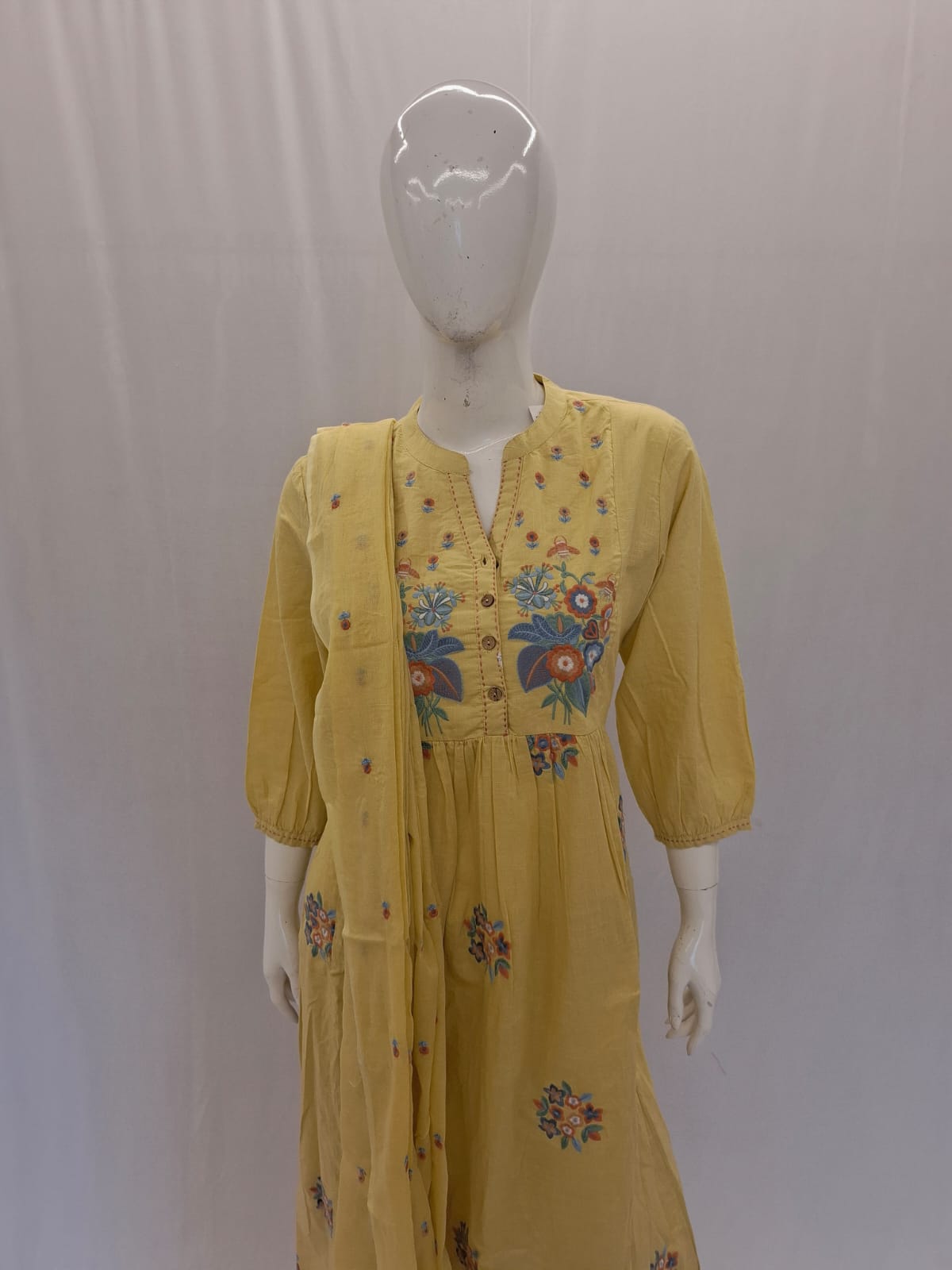 Yellow dress with floral embroidery on a mannequin against a plain background