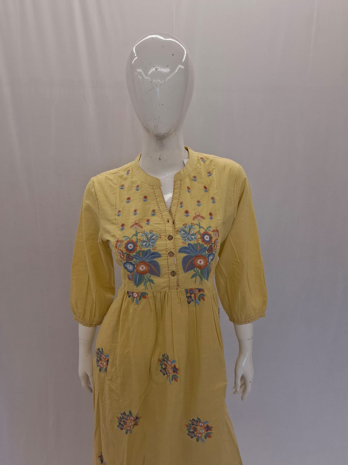Yellow dress with floral embroidery on a mannequin against a plain background