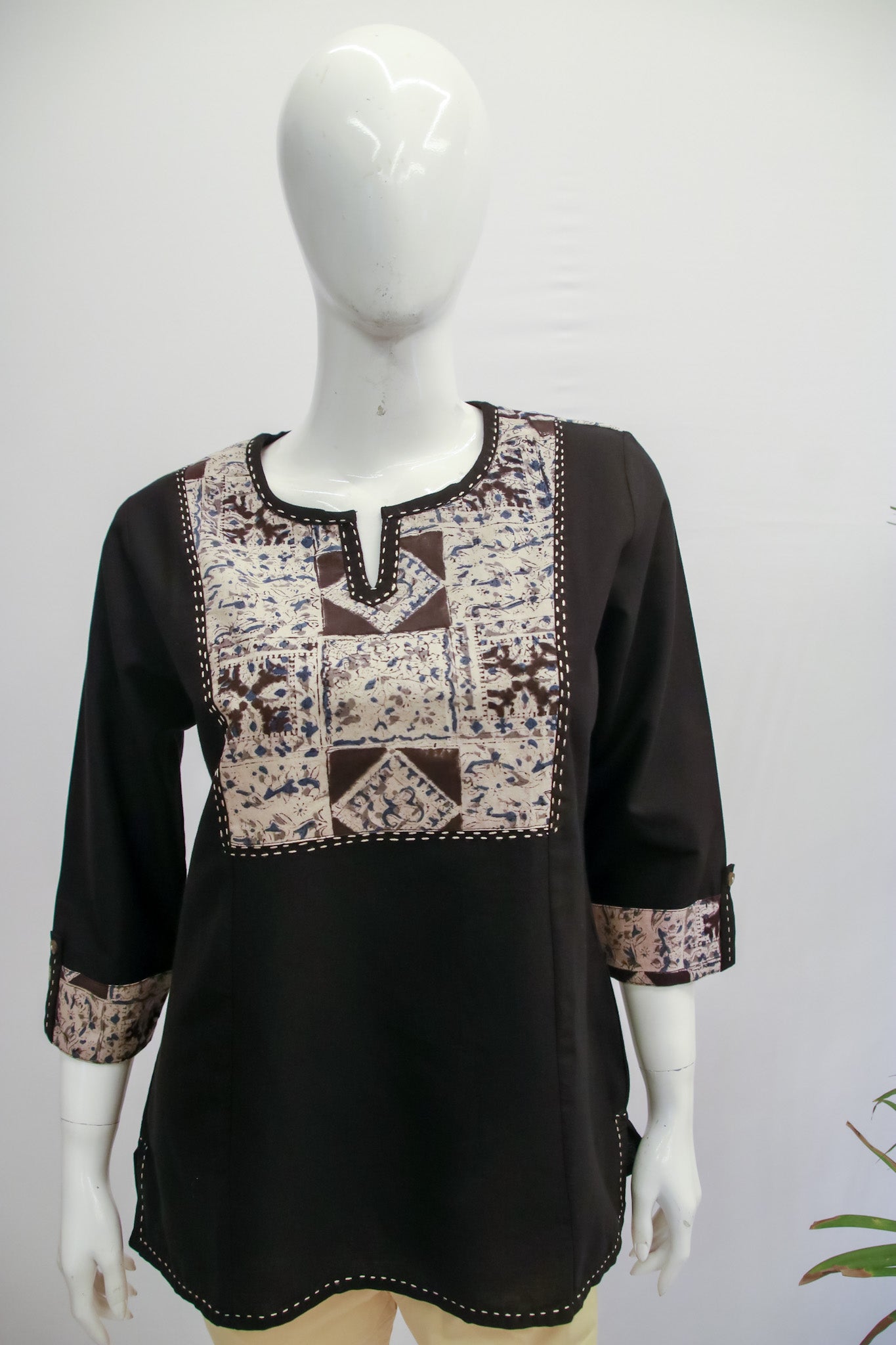 Black blouse with patterned neckline on a mannequin against a white background