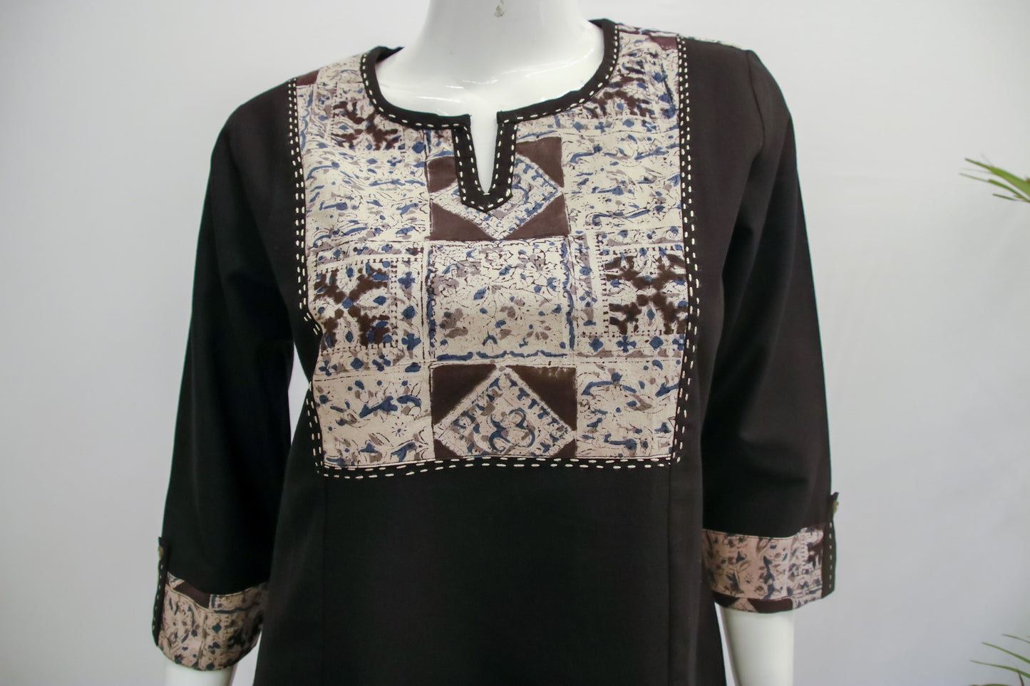 Black long-sleeve top with patterned patchwork design on a mannequin against a white background