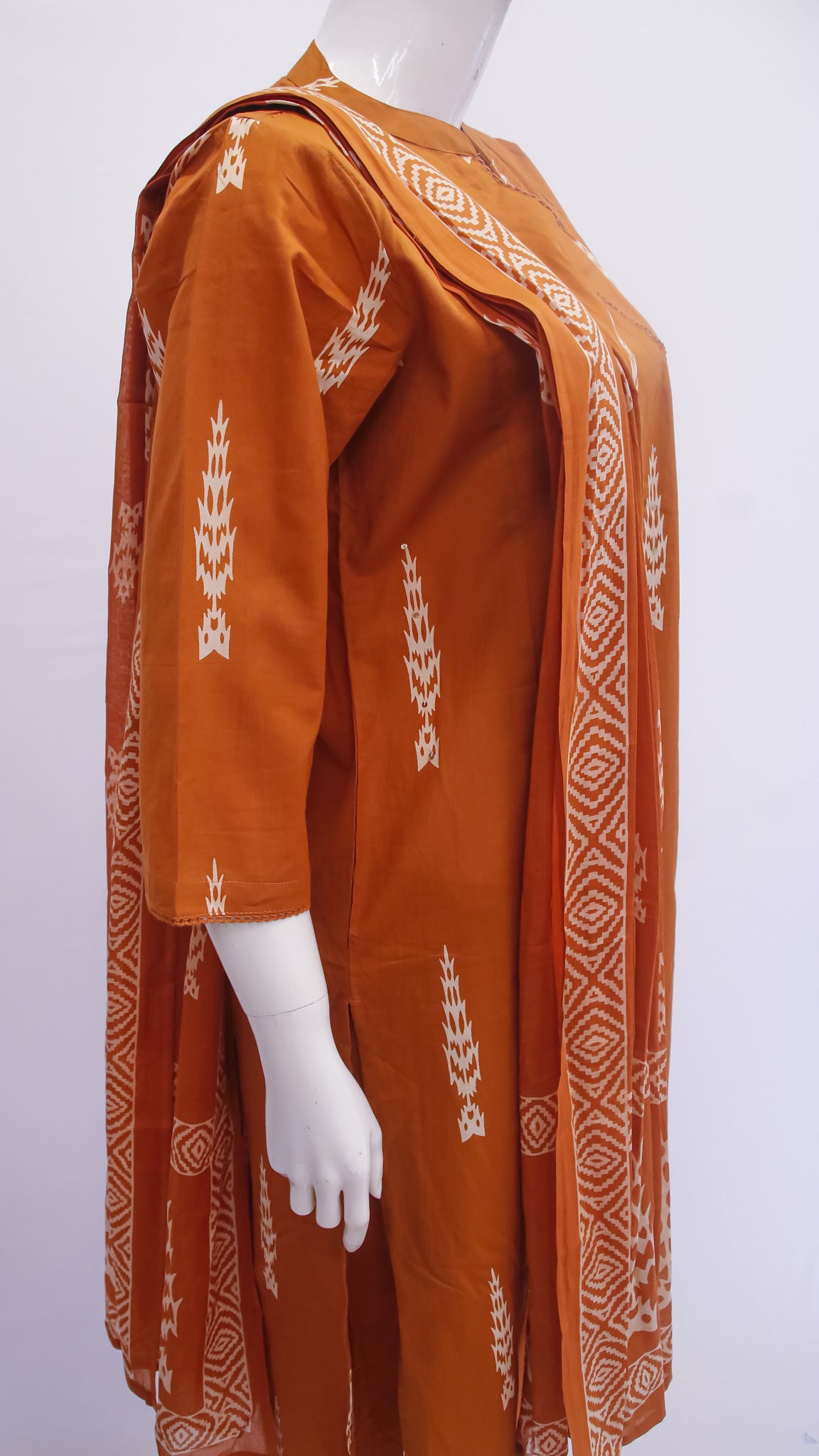 Orange traditional outfit with white patterns on a mannequin against a white background