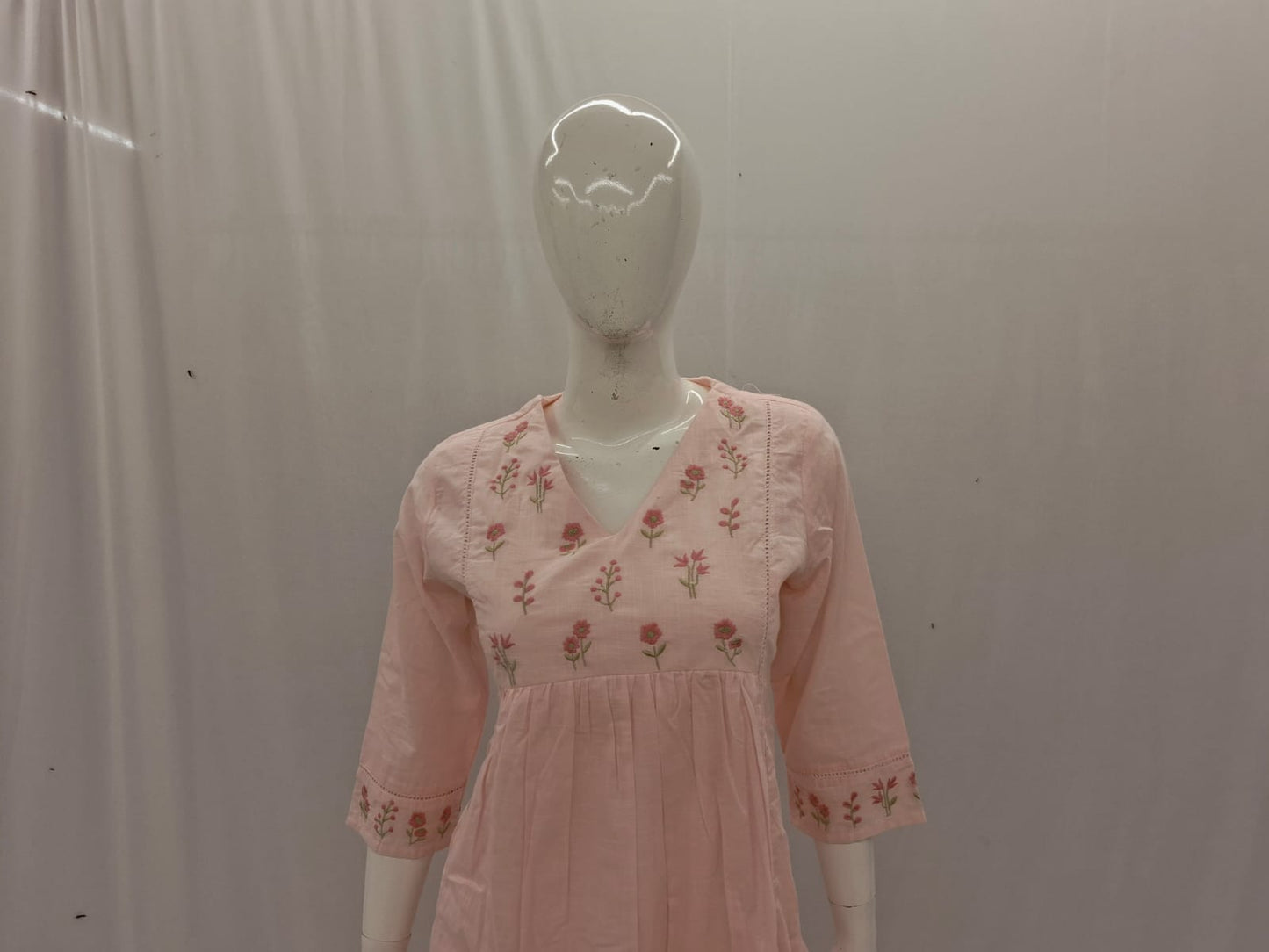 Mannequin wearing a pink dress with floral embroidery against a plain background