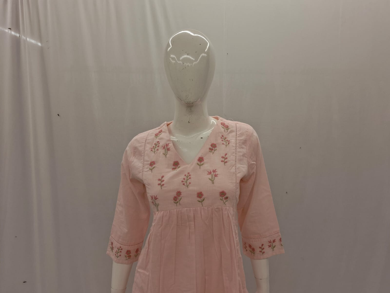 Mannequin wearing a pink dress with floral embroidery against a plain background