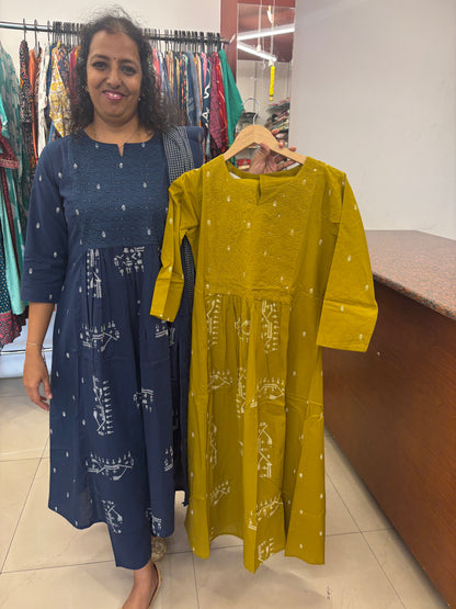 Woman standing next to a rack of yellow and blue dresses in a store.