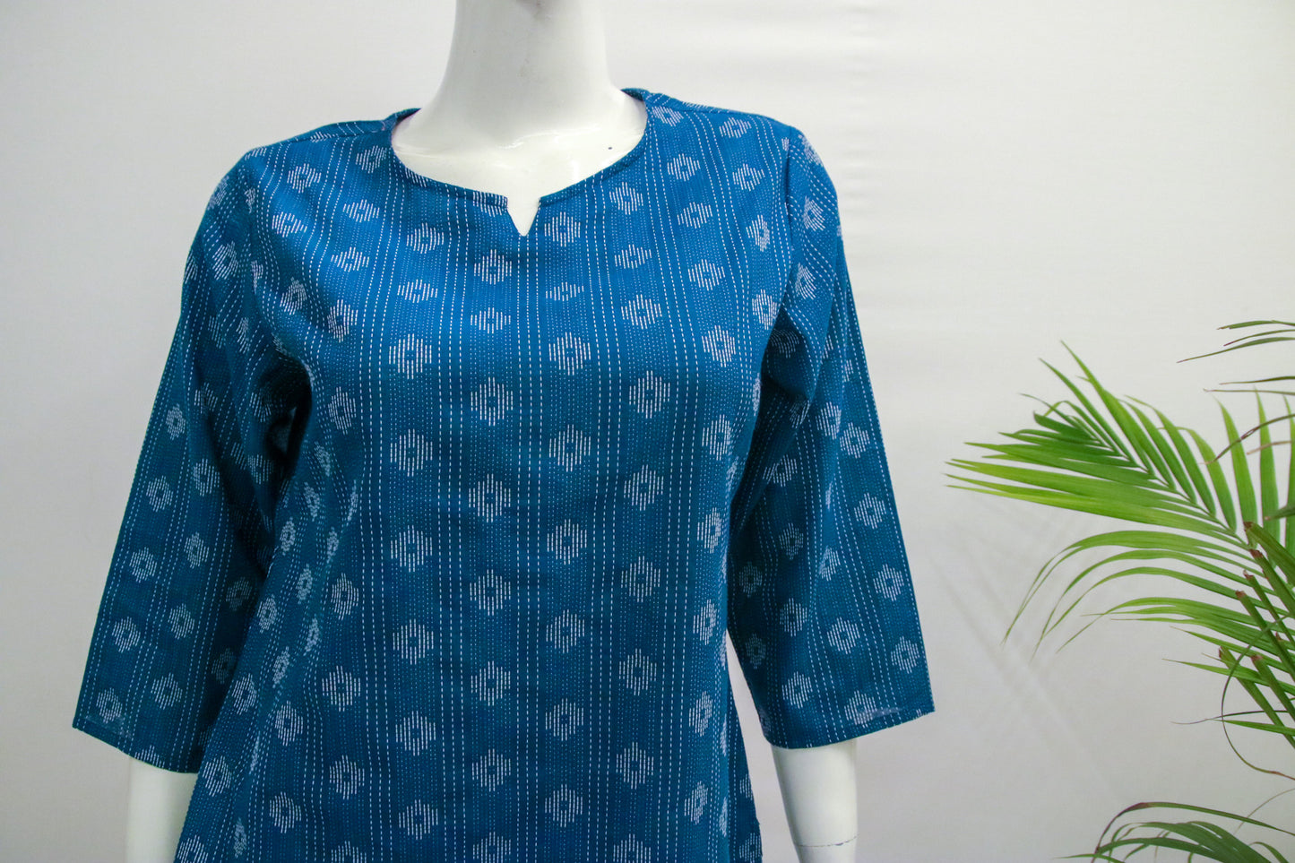 Blue patterned shirt on a mannequin with a white background and green plant