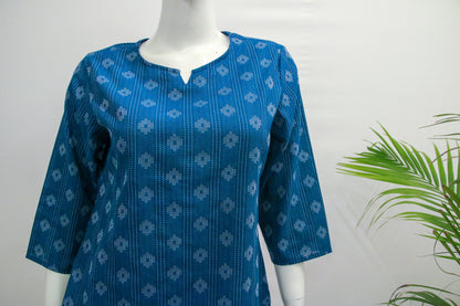 Blue patterned shirt on a mannequin with a white background and green plant