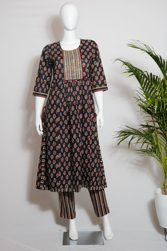 A dark brown cotton top and pant set with a floral print, displayed on a mannequin against a white background, with green leaves in the background.