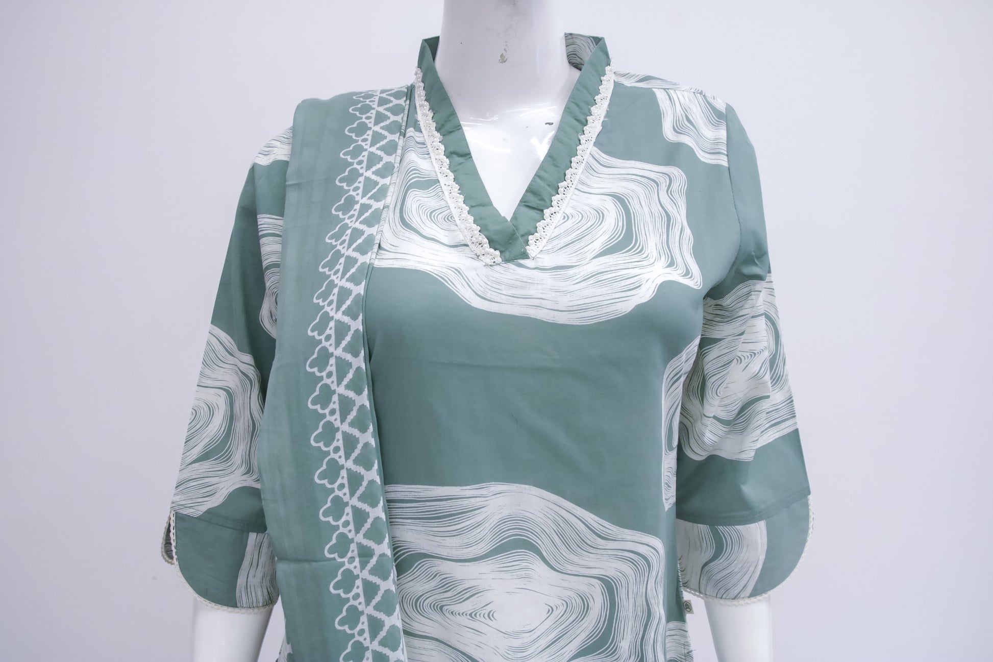 Green blouse with white patterns on a mannequin against a white background