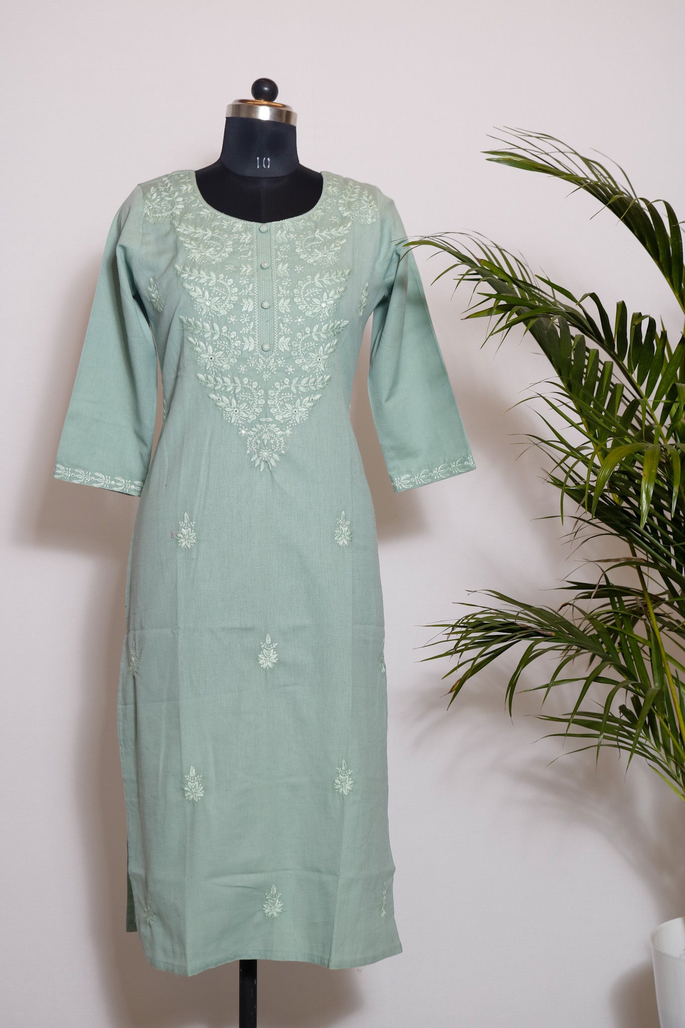 A sea green cotton printed kurta with pocket and chikankari work displayed on a mannequin against a white background, with a plant in the corner.