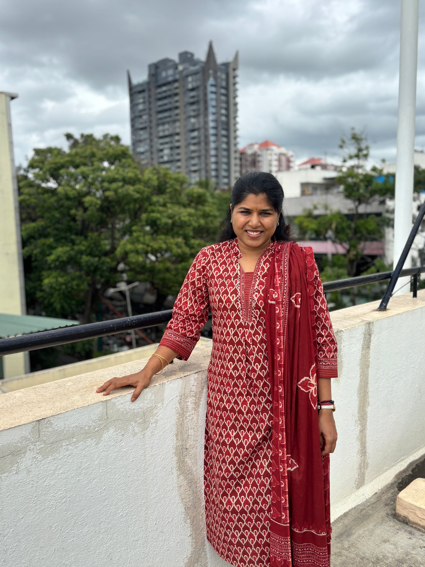 Woman in a red traditional outfit standing on a rooftop with buildings in the background
