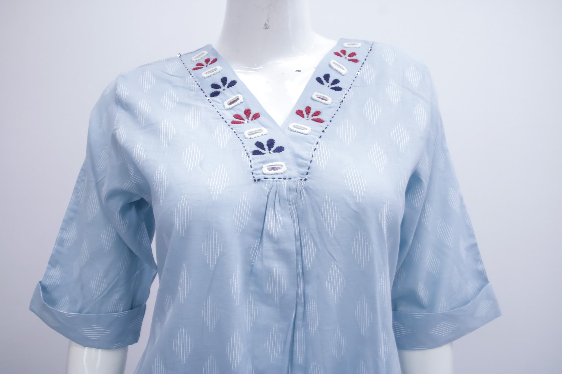 Light blue blouse with floral embroidery on a mannequin against a white background