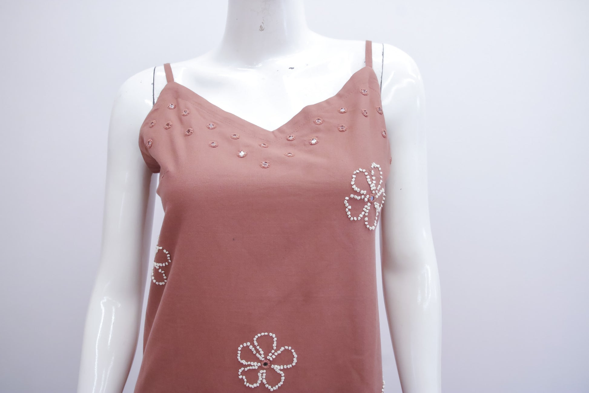 Pink tank top with floral embellishments on a mannequin against a white background
