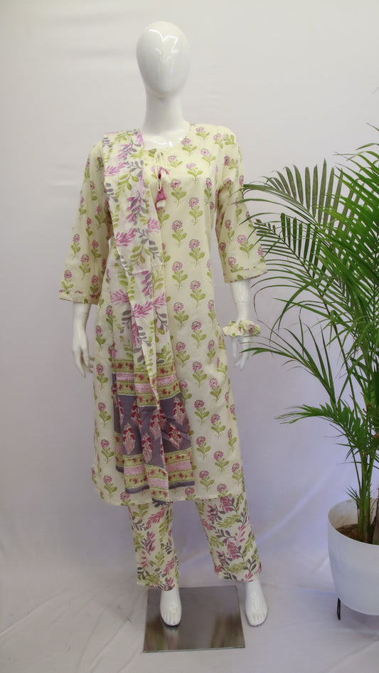 A mannequin displaying a white floral dupatta set with a kurta, pant, and dupatta, standing in a room with a potted plant in the background.