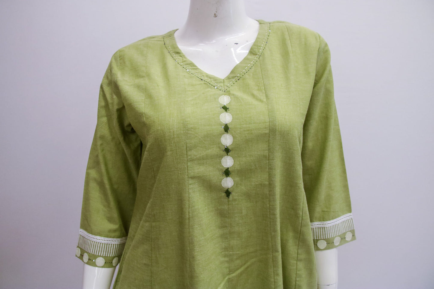 Green blouse with white buttons on a mannequin against a gray background