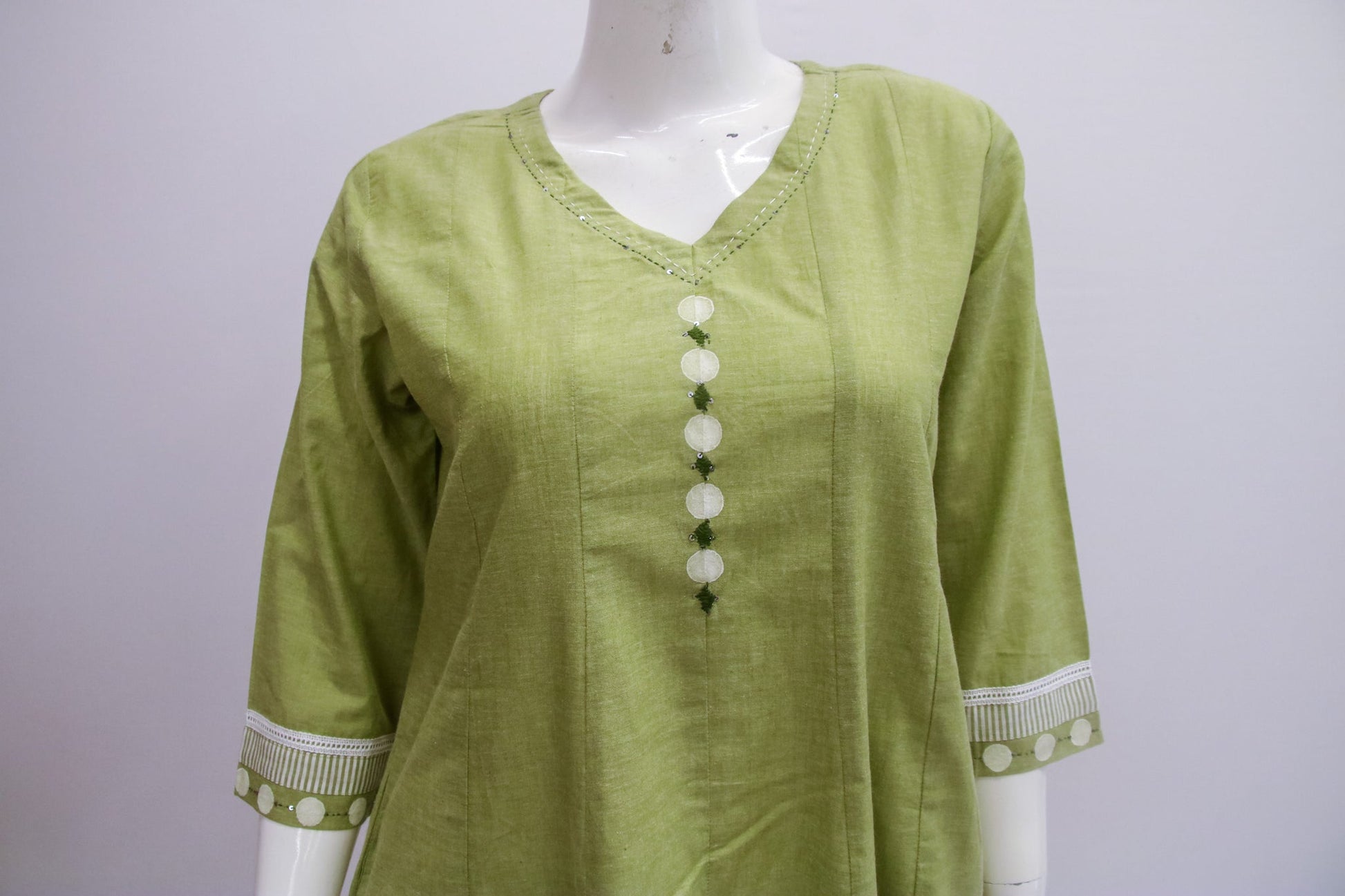 Green blouse with white buttons on a mannequin against a gray background