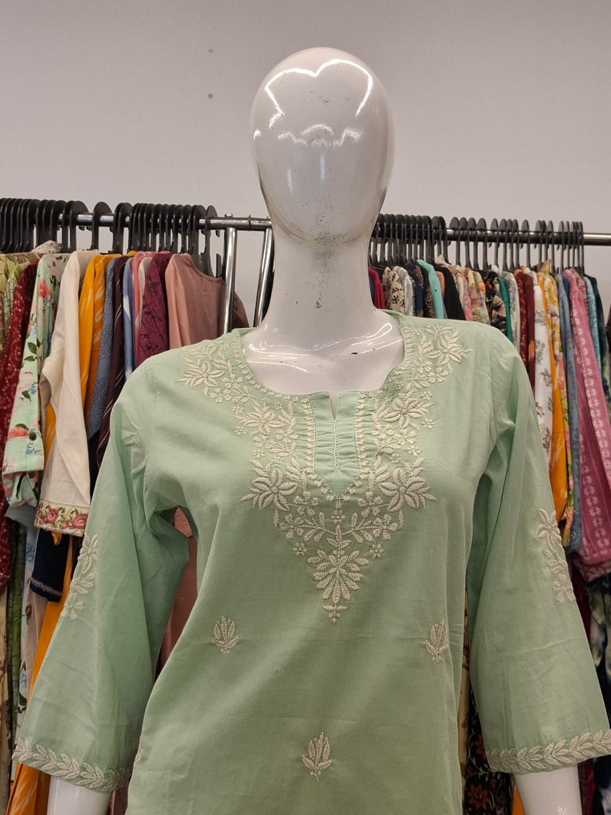 Green embroidered top on a mannequin with a clothing rack in the background